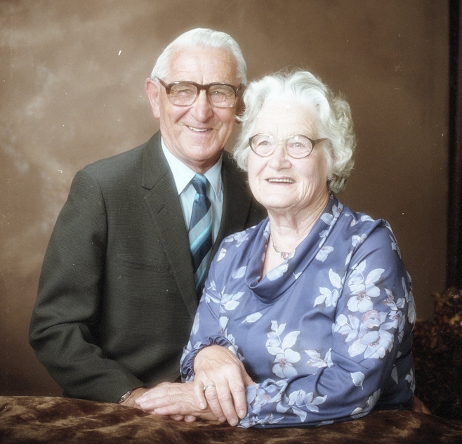 A studio upper-body portrait of the couple sitting close and smiling