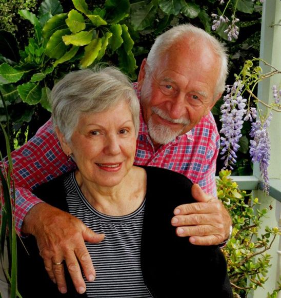 A coloured casual 
photograph of Michał behind Zenona and with his arms around her shoulders. Both have warm smiles. Taken in their garden, the 
background is a wisteria and other creepers.