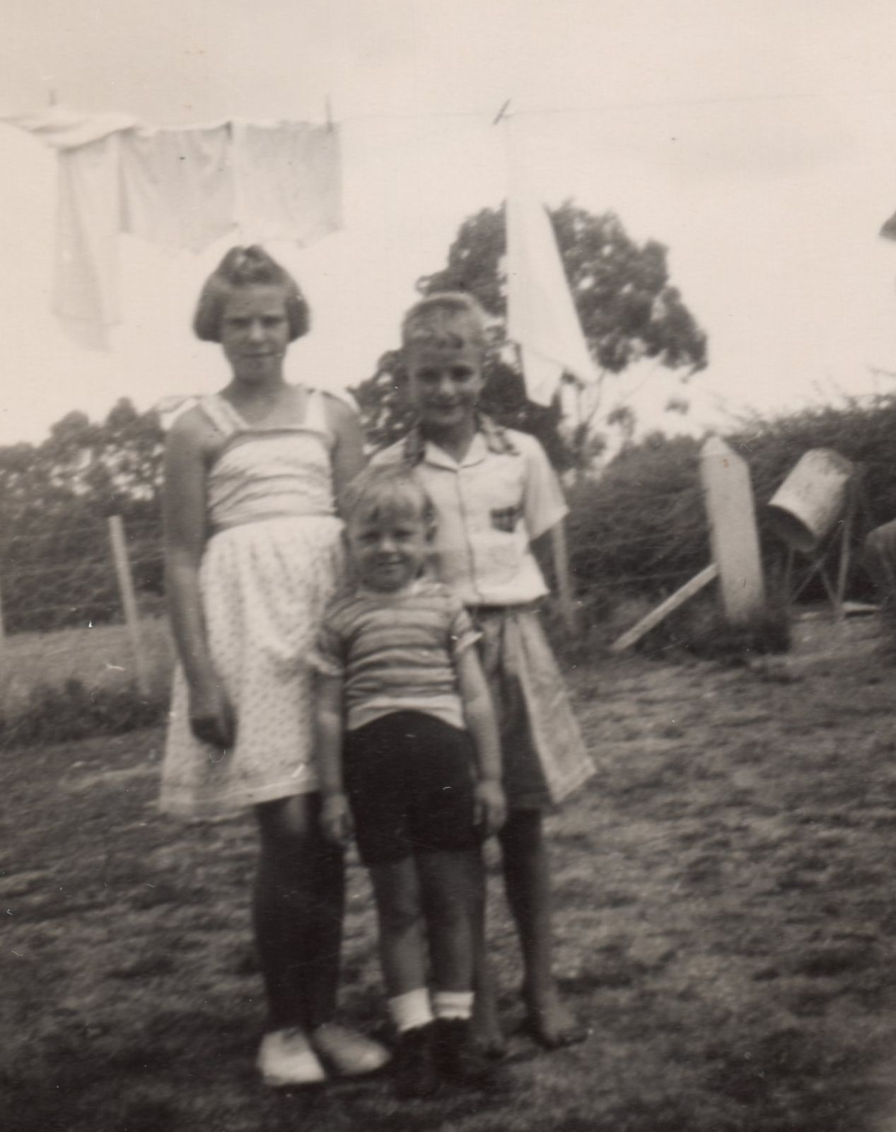 Black 
and white pic of the siblings in the garden, Zenona frowning and in a white sundress, her brothers smiling. Immediately 
behind them is a washline with white laundry.