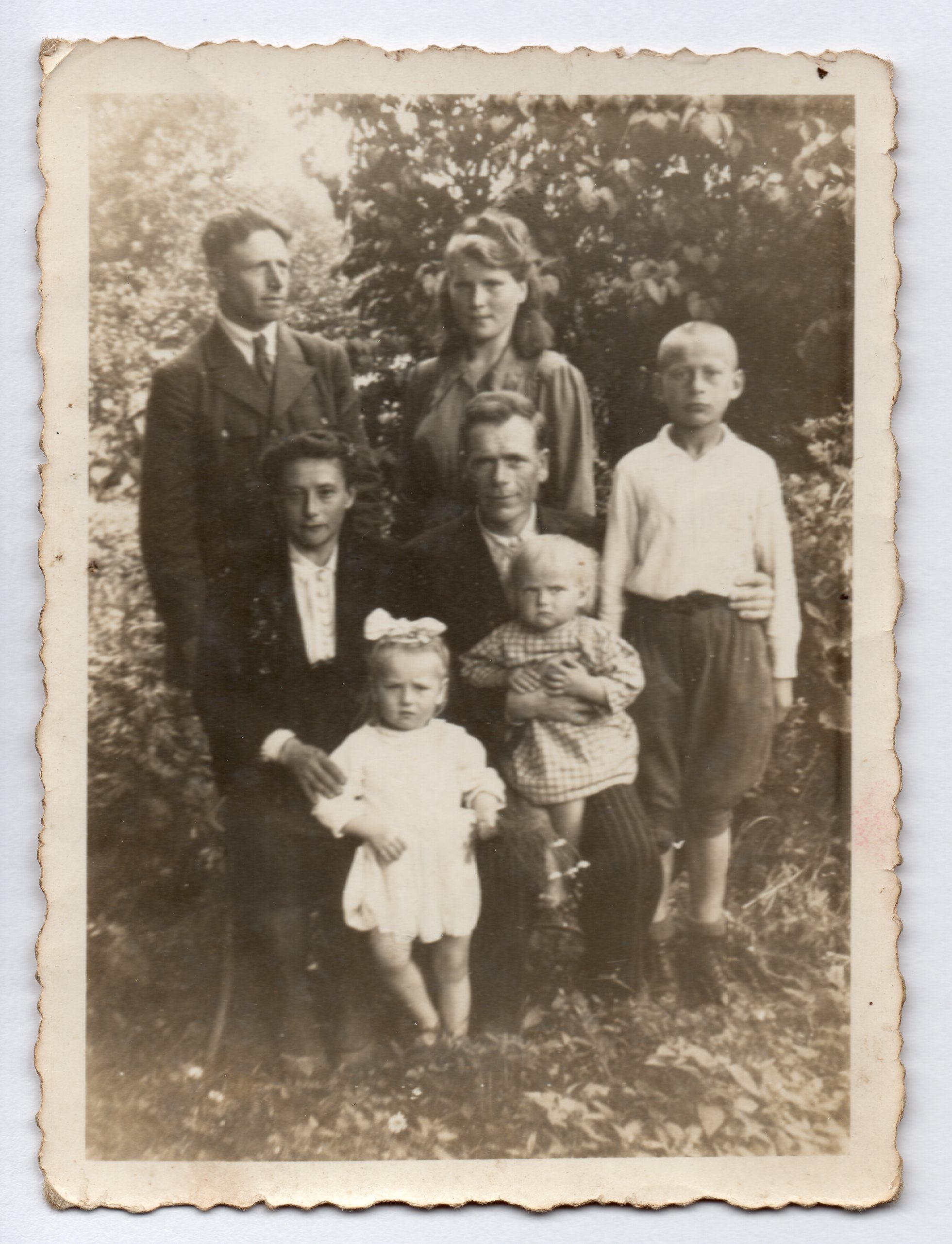 A 
black and white photo of the family around two adults on chairs. All serious. Uncle Józef's hand around Michał's waist is 
clearly seen as he sits with a toddler on his lap next to Michał