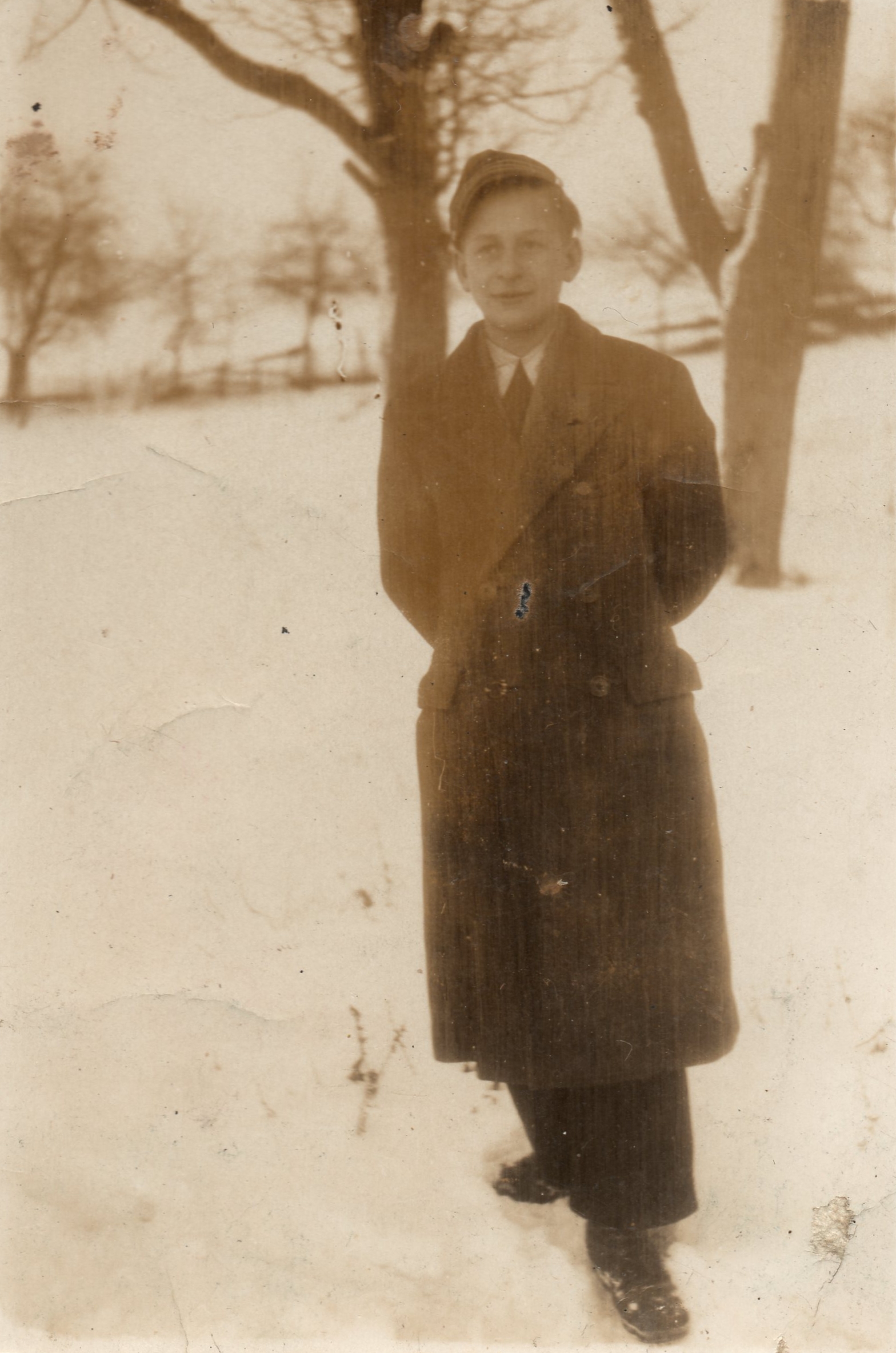 A sepia photograph 
of Michal in a winter coat, standing in a field of snow. Trees in the background.