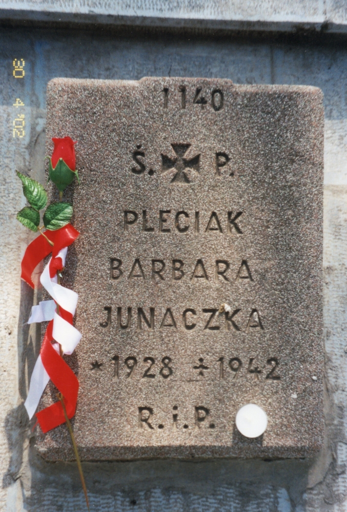 Barbara Pleciak's 
headstone with a red rose, stem wrapped in red and white ribbon