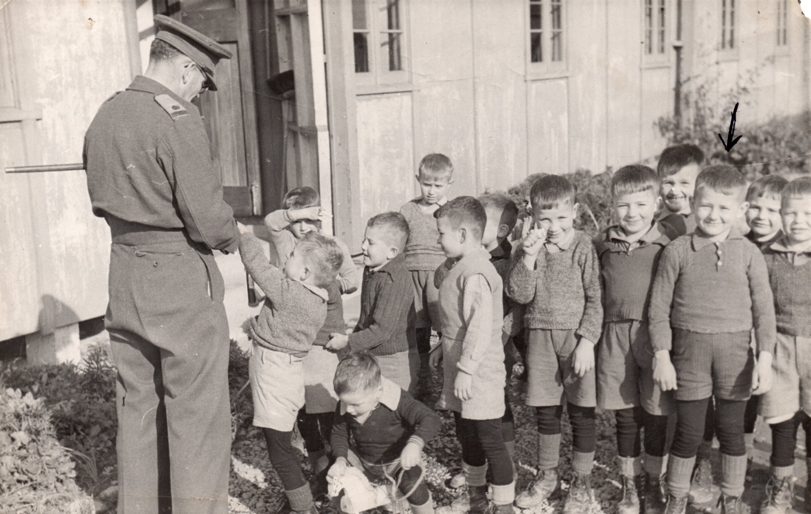 A soldier with 
his back to the camera entertaining a group of boys.