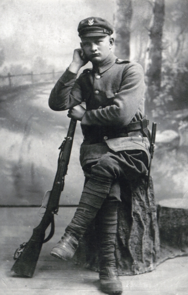 Studio pic of 
Wojciech Pleciak, sitting and leaning on a rifle.