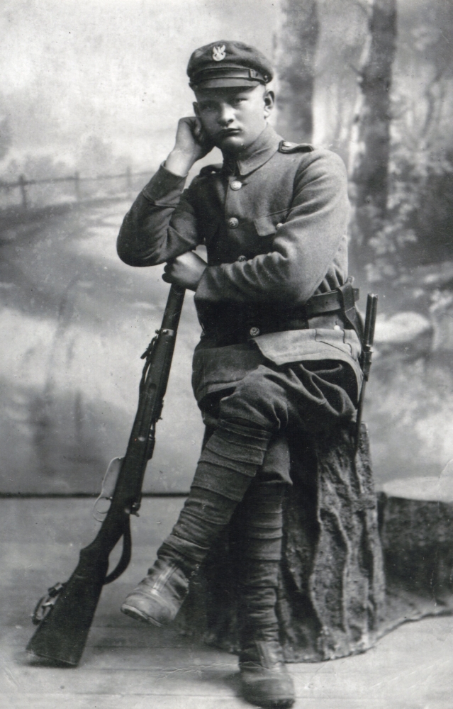 Studio pic of 
Wojciech Pleciak, sitting and leaning on a rifle.