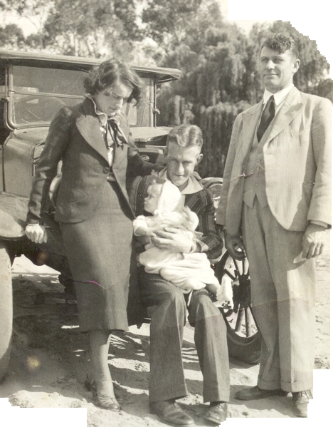 The parents with their son in front of a car. Frank is sitting on the bumper and a man in a light suit is standing 
   next to them looking in the distance towards the left. Frank and Gladys are looking at the infant.