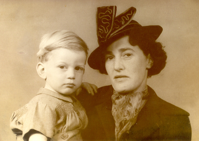 A sepia head and shoulders studio photograph of a sombre Gladys in smart coat and hat holding an equally sombre 
   Trevor