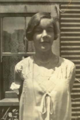 waist-up sepia photograph of a teenaged girl in a Sunday-best dress, taken outside, in front of a window