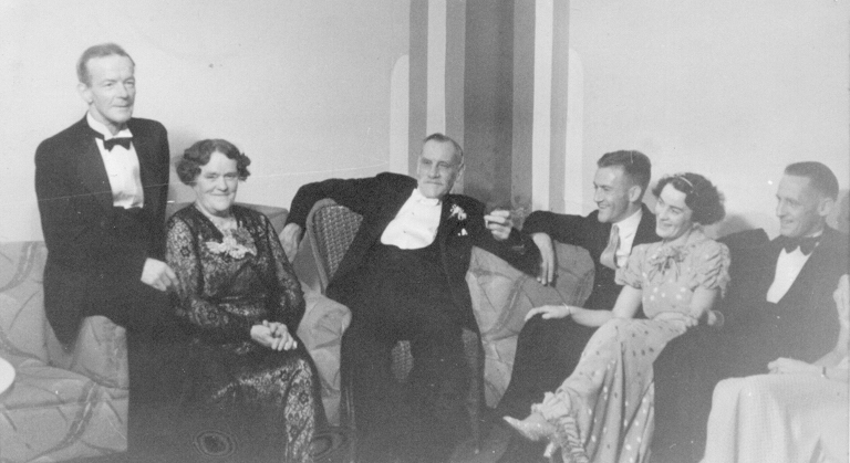 black and white photograph of a group of people in evening wear sitting on armchairs.