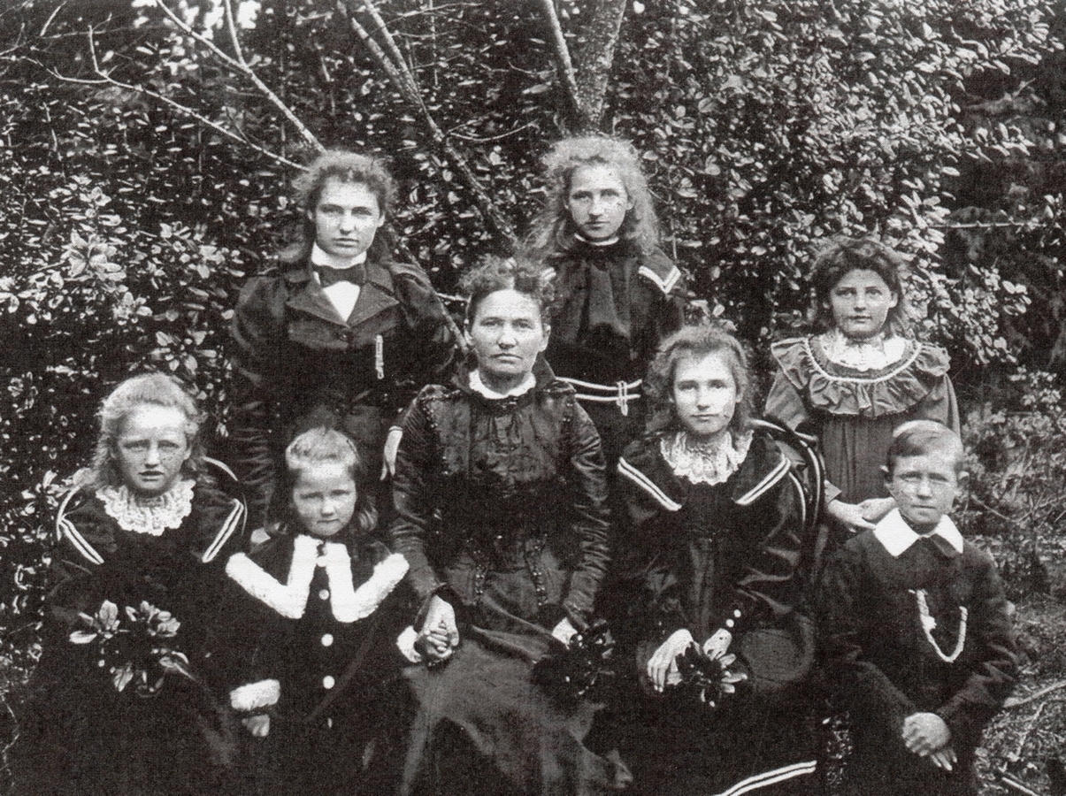 Julianna 
sitting in a garden with seven of her children. All are wearing formal attire. All serious.