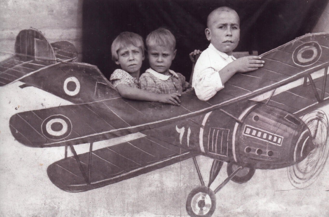 Danuta, Alina and 
Tadeusz as the pilot in front, all looking very serious, sitting within a cut-out aeroplane.