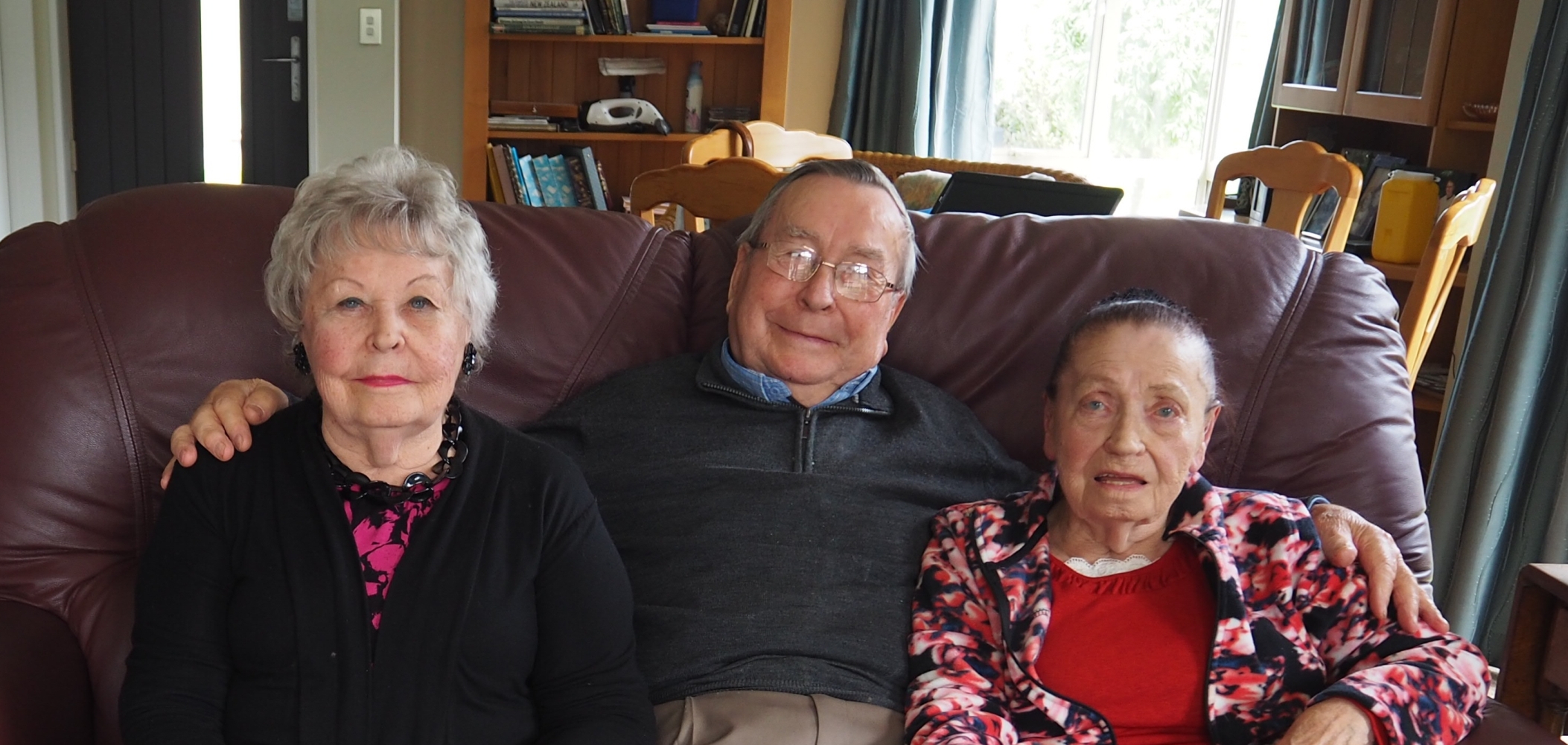 Tadeusz seated between his 
sisters, on a couch in his lounge.