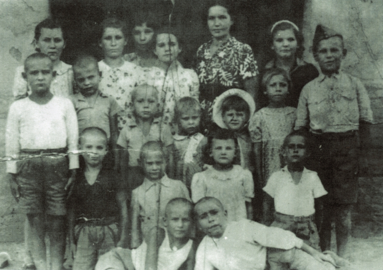 A group of Polish 
children, with a woman. Alina, Danuta and Tadeusz are wearing the same clothes as the previous photograph.