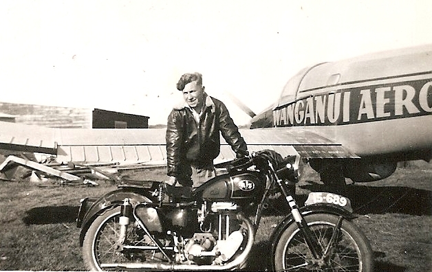 Kazik behind his motorbike, in leather jacket, and part of an aeroplane with Wanganui Aero written on the side.