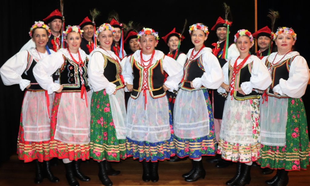 The 14 members of the group in colourful national costume, posing hands on hips and smiling broadly.