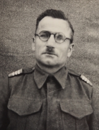 A uniformed man in his late 40s round glasses, dark hair.