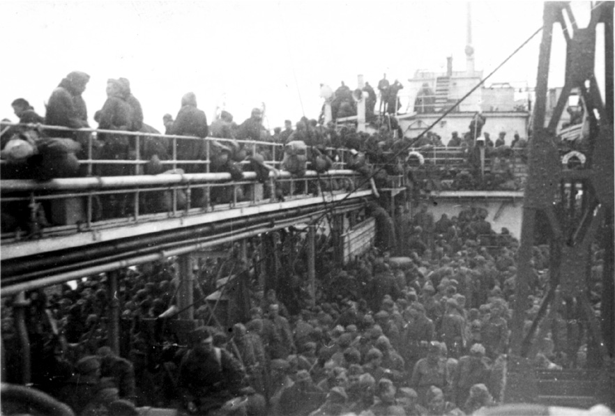 The deck and parts of a bridge on a ship, filled with throngs of people.